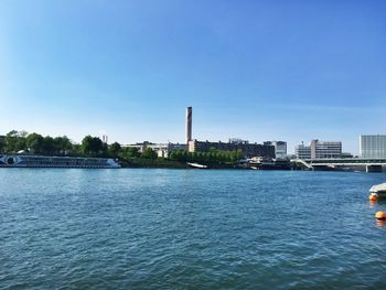 Scenic view of river by buildings against clear blue sky