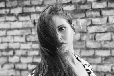 Portrait of confident woman standing against brick wall