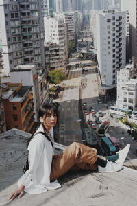 Woman sitting on sidewalk against buildings in city