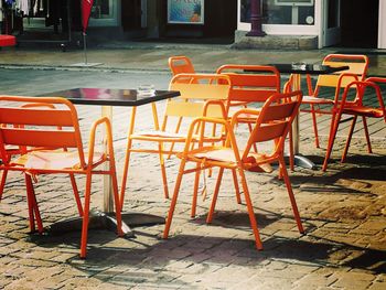 Empty chairs and tables at sidewalk cafe by building