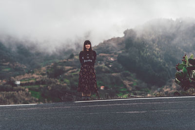 Young woman standing on road against mountain during foggy weather