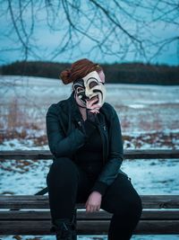 Woman holding mask over face while sitting on bench