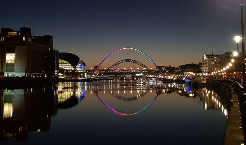 Illuminated bridge over river against sky in city at night