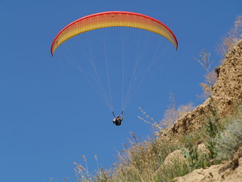 Low angle view of paragliding against clear blue sky