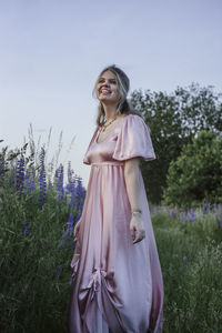 Woman standing by purple flower on field against sky