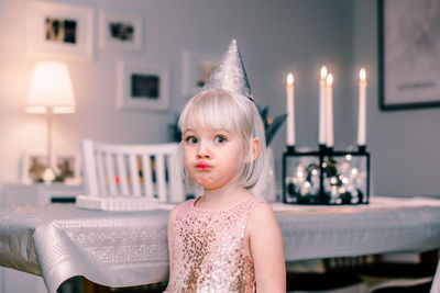 Portrait of girl wearing party hat making face while standing at home