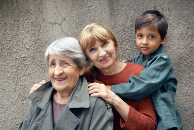 Three generations grandmother great grandmother grandson are standing on the street against a gray 