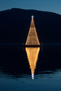 Illuminated gazebo by lake against sky at night