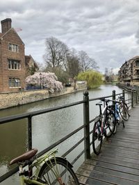 Bicycle parked by canal against sky in city
