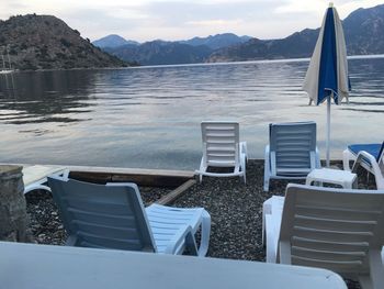 Empty chairs by lake against sky