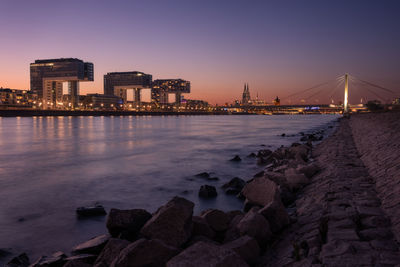 View of illuminated buildings by sea against sky at sunset