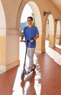 Young caucasian man sitting outdoor near electric scooter and drinking coffee to-go