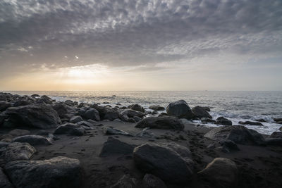 Rocks on beach against sky during sunset