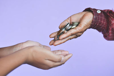 Cropped image of father giving coins to son against purple background