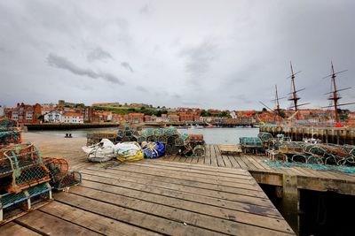 Boats moored at harbor in city against sky