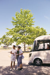 Father and children reading map while woman sitting in camper trailer at park