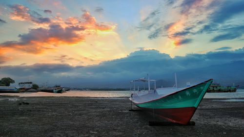 Boat moored on beach against sky during sunset