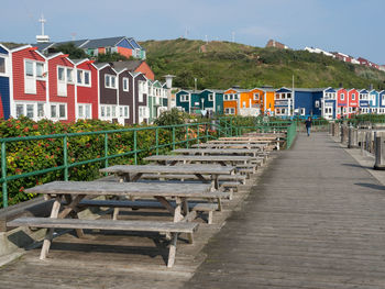 Empty benches by buildings against sky in town