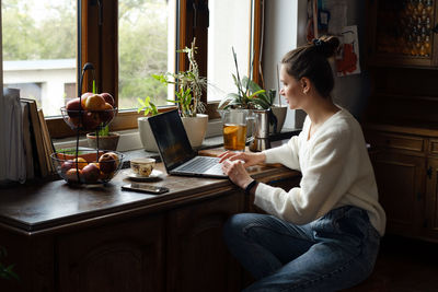 Young freelancer working on laptop at home. woman using computer on the kitchen for work. distant