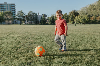 Boy playing with ball on grassy land in park