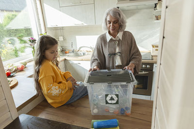 Grandmother and granddaughter sorting recycling waste in kitchen