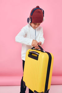 Boy carrying suitcase against colored background