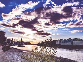 Bridge over river by buildings against sky during sunset