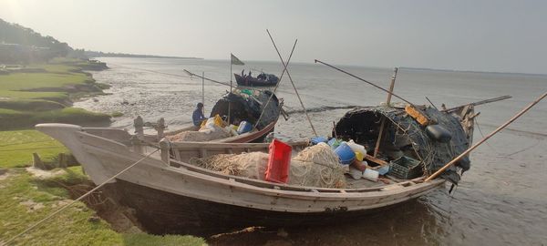 Fishing boats on sea shore against sky