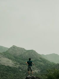 Rear view of man standing on mountain against sky