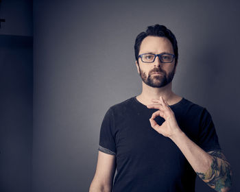 Portrait of man gesturing ok sign while standing against wall