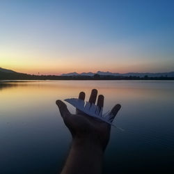 Midsection of person by lake against sky during sunset