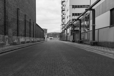 Empty road by buildings against sky in city