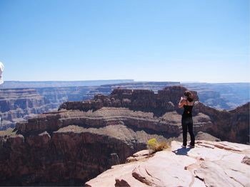 Rear view of woman photographing while standing at grand canyon on against sky during sunny day