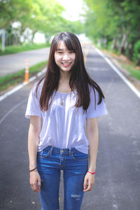 Portrait of smiling young woman standing on road in city