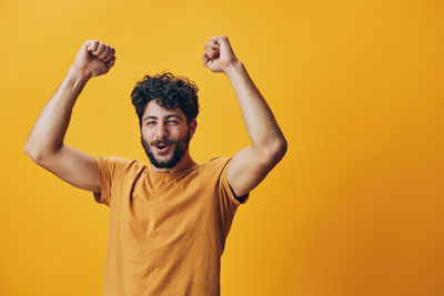 Rear view of man with arms raised standing against yellow background