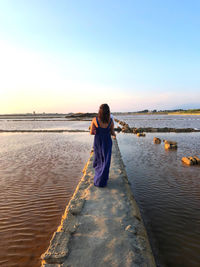 Rear view of woman standing on pier by water against sky