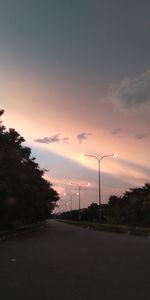 Street amidst field against sky at sunset