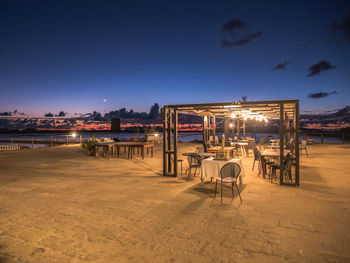 Chairs and tables at beach against sky at night