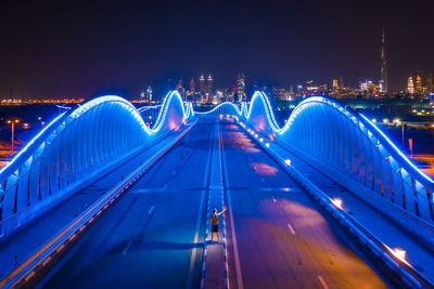 Light trails on bridge in city against blue sky