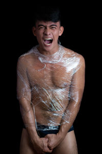 Midsection of shirtless man standing against black background