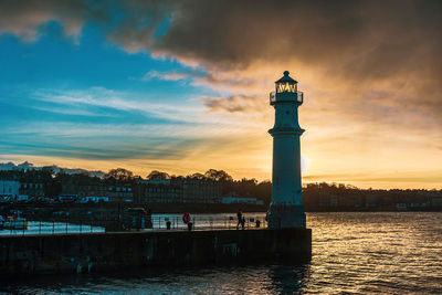 Lighthouse by sea against sky during sunset