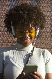 Cool young latin american woman with afro hair and glasses smiling using smartphone 