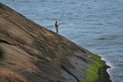 Rear view of woman standing on rock by sea