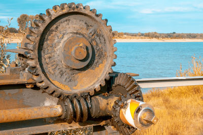 Close-up of rusty machine part by sea against sky