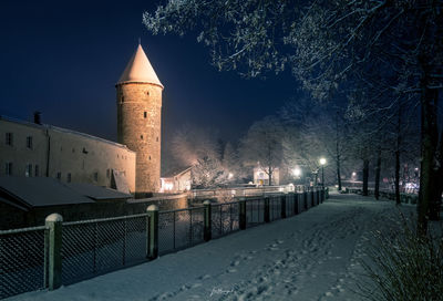 Illuminated street amidst buildings against sky at night during winter