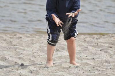 Low section of person playing with sand at beach