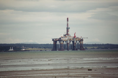 Oil drill amidst sea against sky