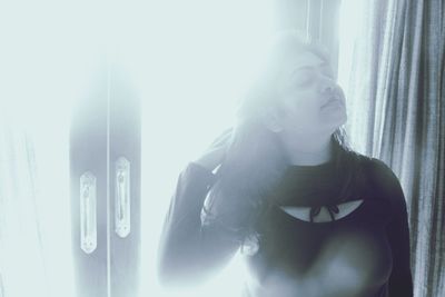 Portrait of young woman looking through window at home