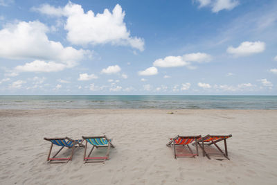 Deck chairs on beach against sky