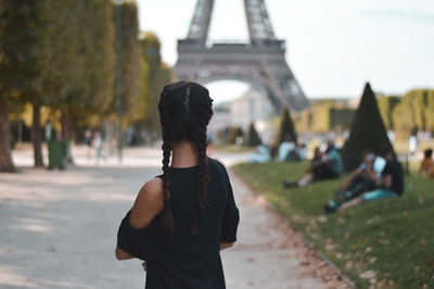 Rear view of woman standing on road against eiffel tower in city